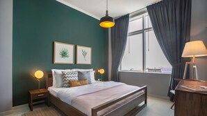 Ein Schlafzimmer mit einem Bett, zwei Nachttischen, einem Fenster mit Vorhängen und Blick auf die Stadt.