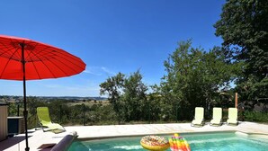 Piscina con sillas de descanso y una sombrilla, rodeada de árboles y vistas al campo.