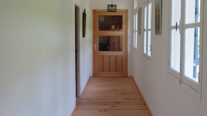 Un pasillo estrecho con suelo de madera, paredes blancas y una puerta de madera al final.