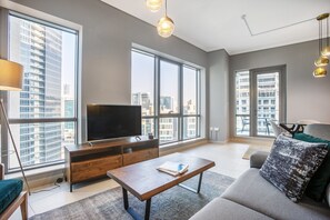 A modern living room with large windows, a flat-screen TV, a wooden coffee table, and a sofa with cushions.