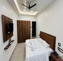 Una habitación de hotel con cama, ventilador de techo, televisión montada en la pared y armario de madera.