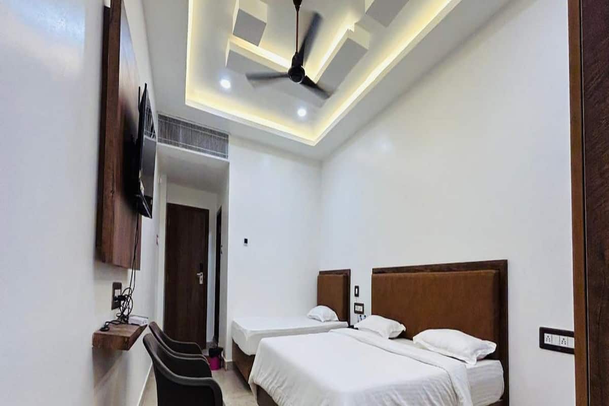 Een hotelkamer met een bed, een bureau, een stoel, een plafondventilator en een aan de muur bevestigde televisie.