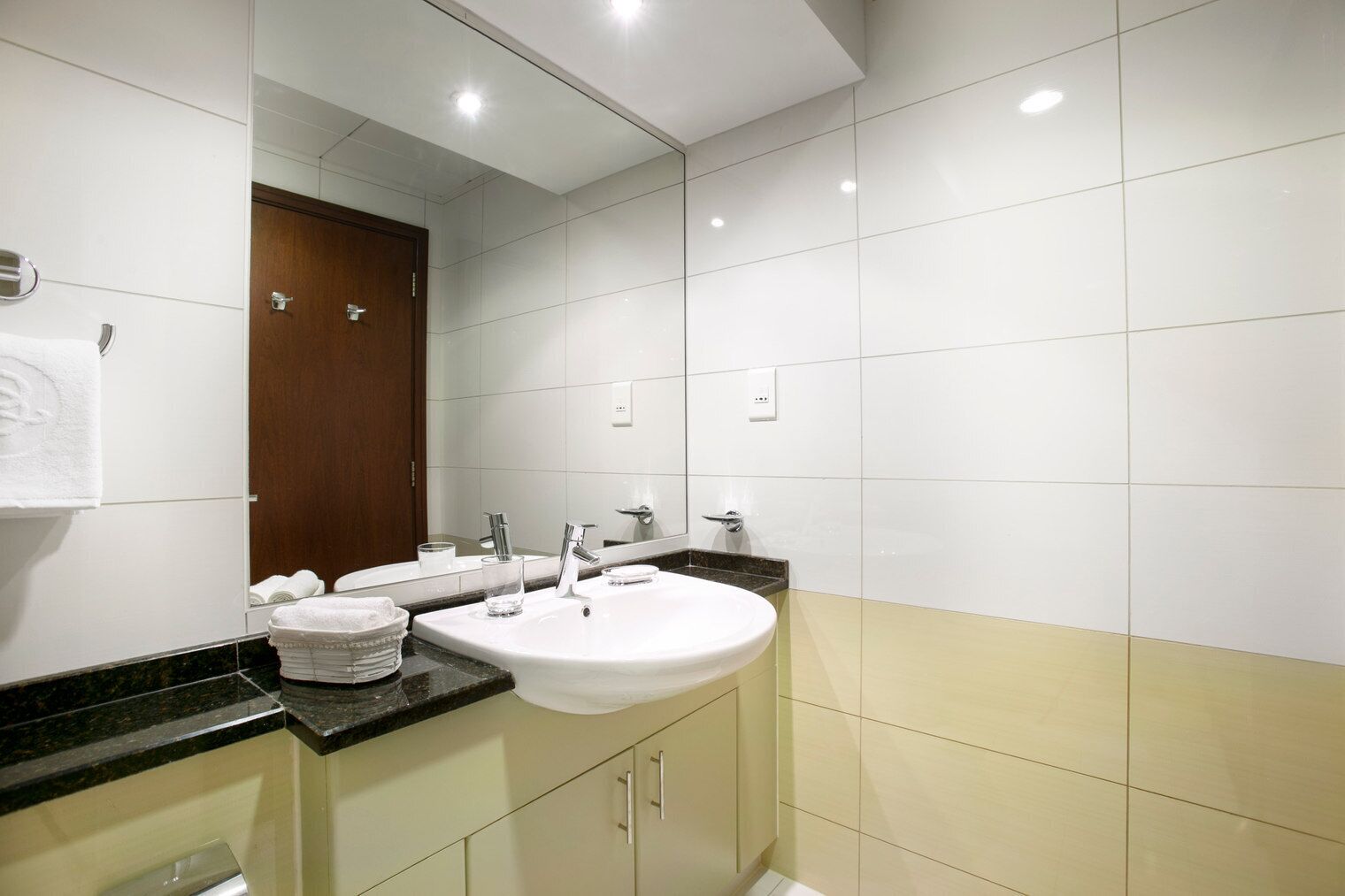 Une salle de bain moderne avec un grand miroir, deux lavabos et une porte en bois.
