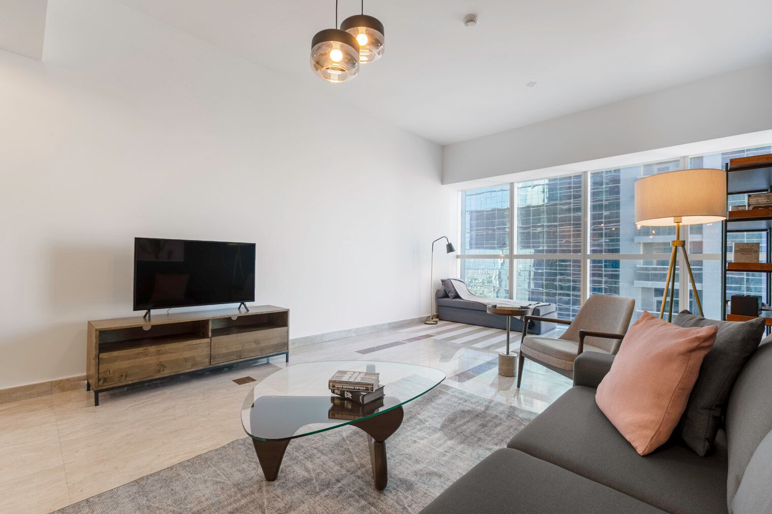 Ein modernes Wohnzimmer mit Flachbildfernseher, Glastisch, Sofa und einem großen Fenster mit Blick auf die Stadt.