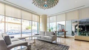 A modern lobby with a grey sofa, two round tables, and a patterned rug. - Blueground | Dubai Marina, shared pool, nr Beach (Dubai)