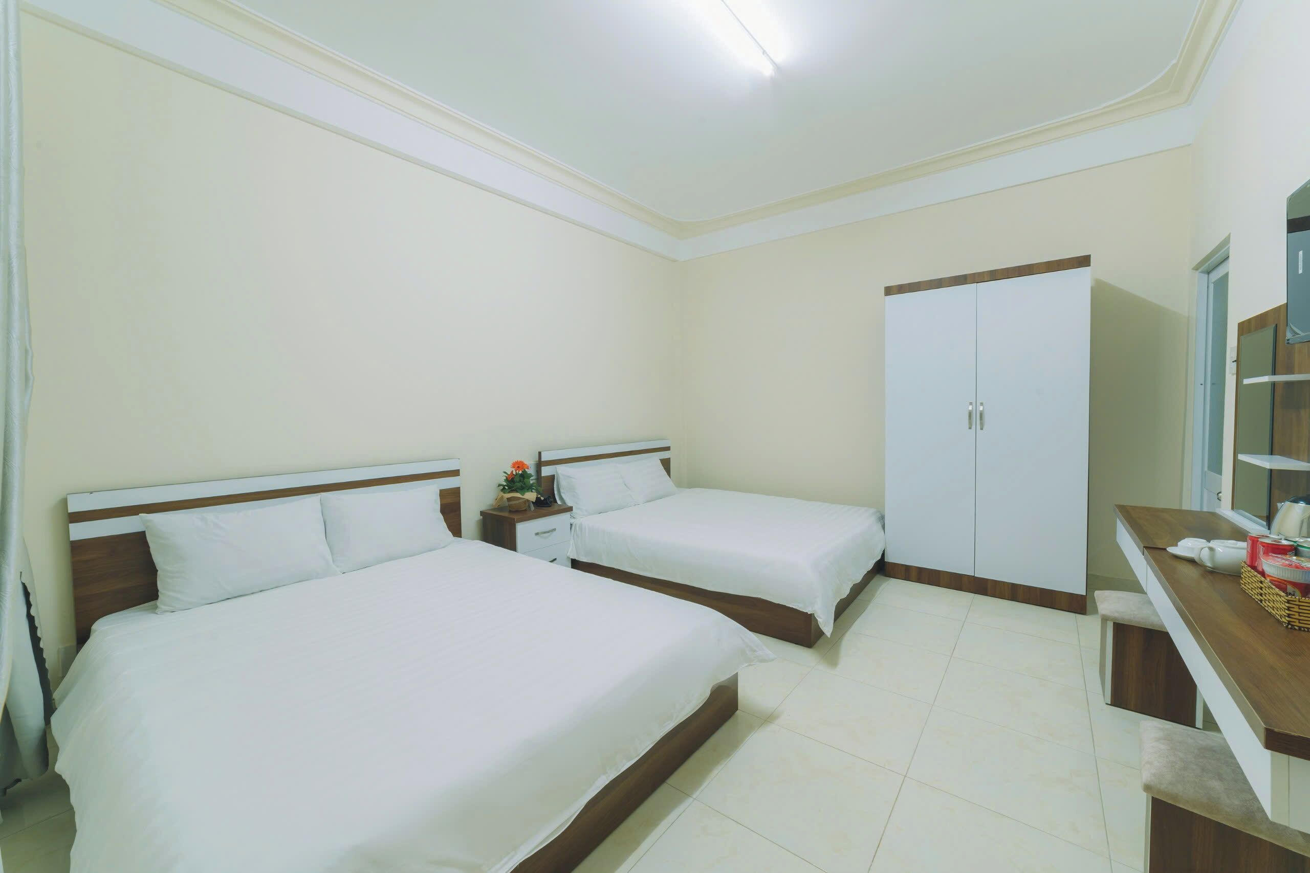 A hotel room with two beds, a wardrobe, a desk with a mirror, and a small table with a basket.