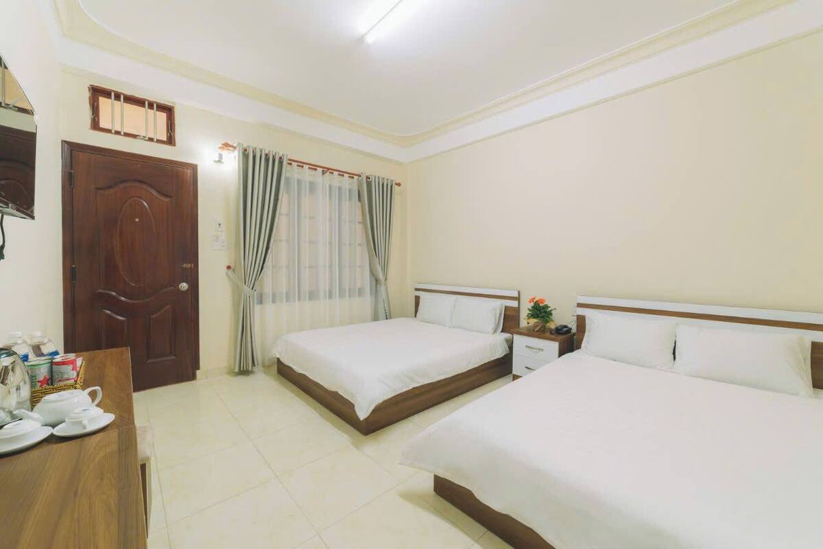 Une chambre d’hôtel avec deux lits simples, une armoire en bois, une table de chevet avec une lampe et une fenêtre avec des rideaux.