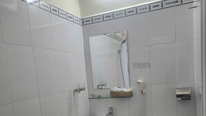 A small, clean bathroom with white tiles, a white sink, a toilet, and a glass shelf above the sink. - Phat Loi Hotel Dalat  (Xuan Huong - Da Lat)