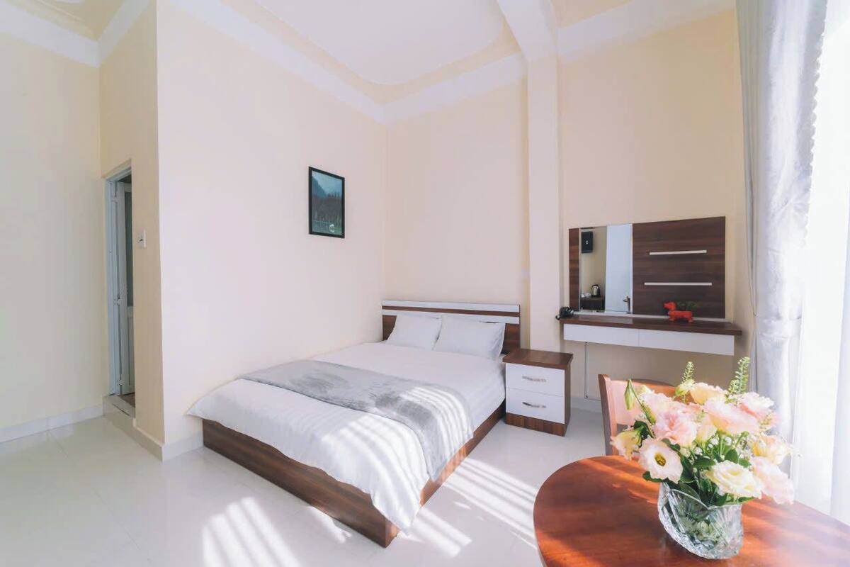 Une chambre à coucher comprenant un lit, une table de chevet, une commode, une coiffeuse avec un miroir et un vase avec des fleurs.