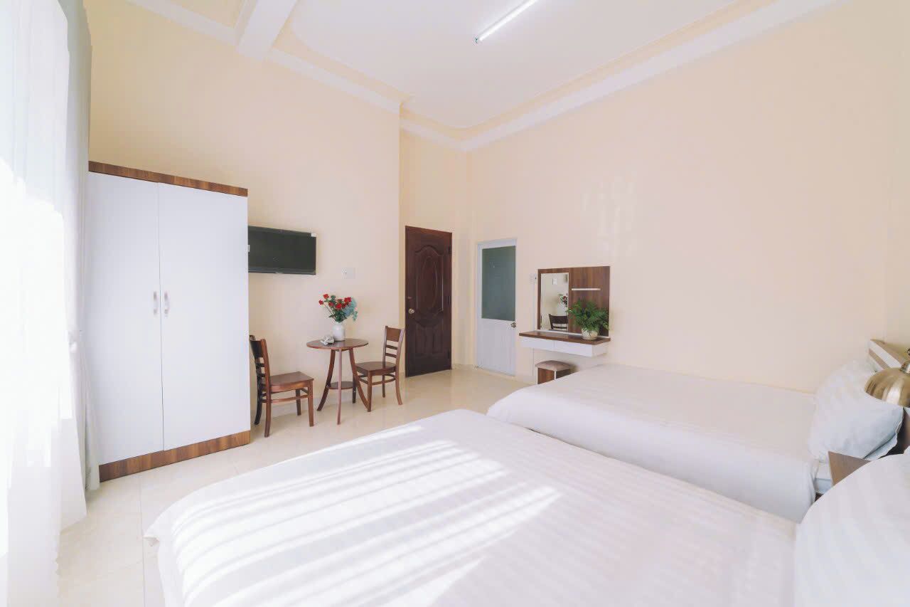 Een hotelkamer met een groot bed, een bureau met stoel, een kledingkast en een kleintje tafeltje met een bloemenvaas.