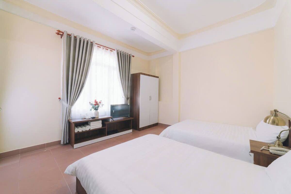 Une chambre d’hôtel avec deux lits, une télévision, une armoire et un bureau avec une lampe.