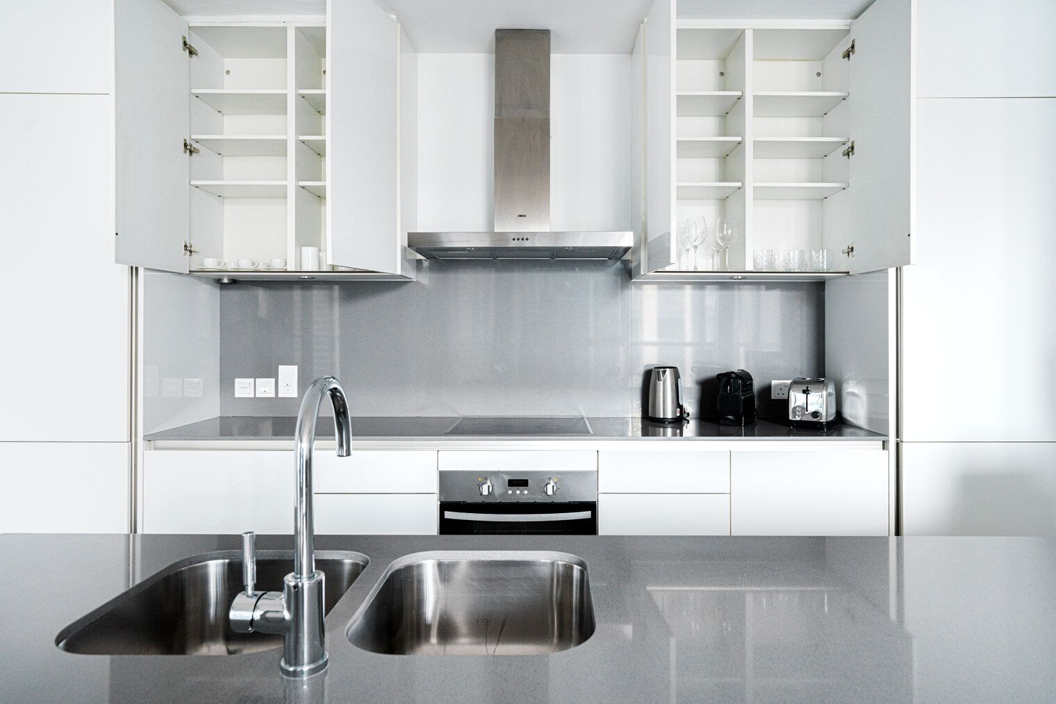 Una cucina moderna con elettrodomestici in acciaio inossidabile, un lavello doppio e mensole a vista.