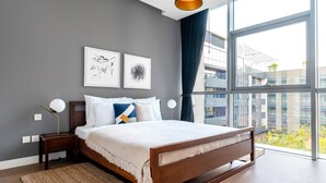 A modern bedroom with a large bed, two bedside tables, a floor lamp, and a view of a cityscape through large windows. - Blueground | City Walk, pool, nr City Park (Dubai)