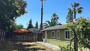Un patio trasero residencial con un porche, una valla de madera y altas palmeras.