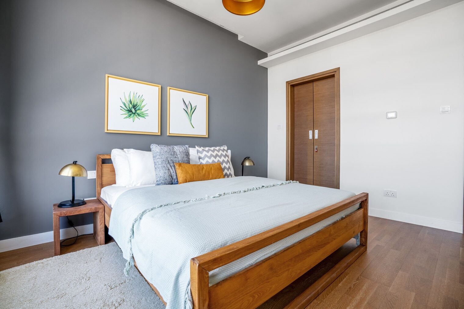 Une chambre à coucher avec un lit en bois, une table de chevet avec une lampe, une armoire et deux reproductions botaniques encadrées accrochées au mur.