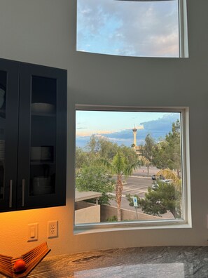 Enjoy a city view from the large window, featuring a prominent tower. The room includes a dark cabinet and a cozy seating area with a chair and a book.