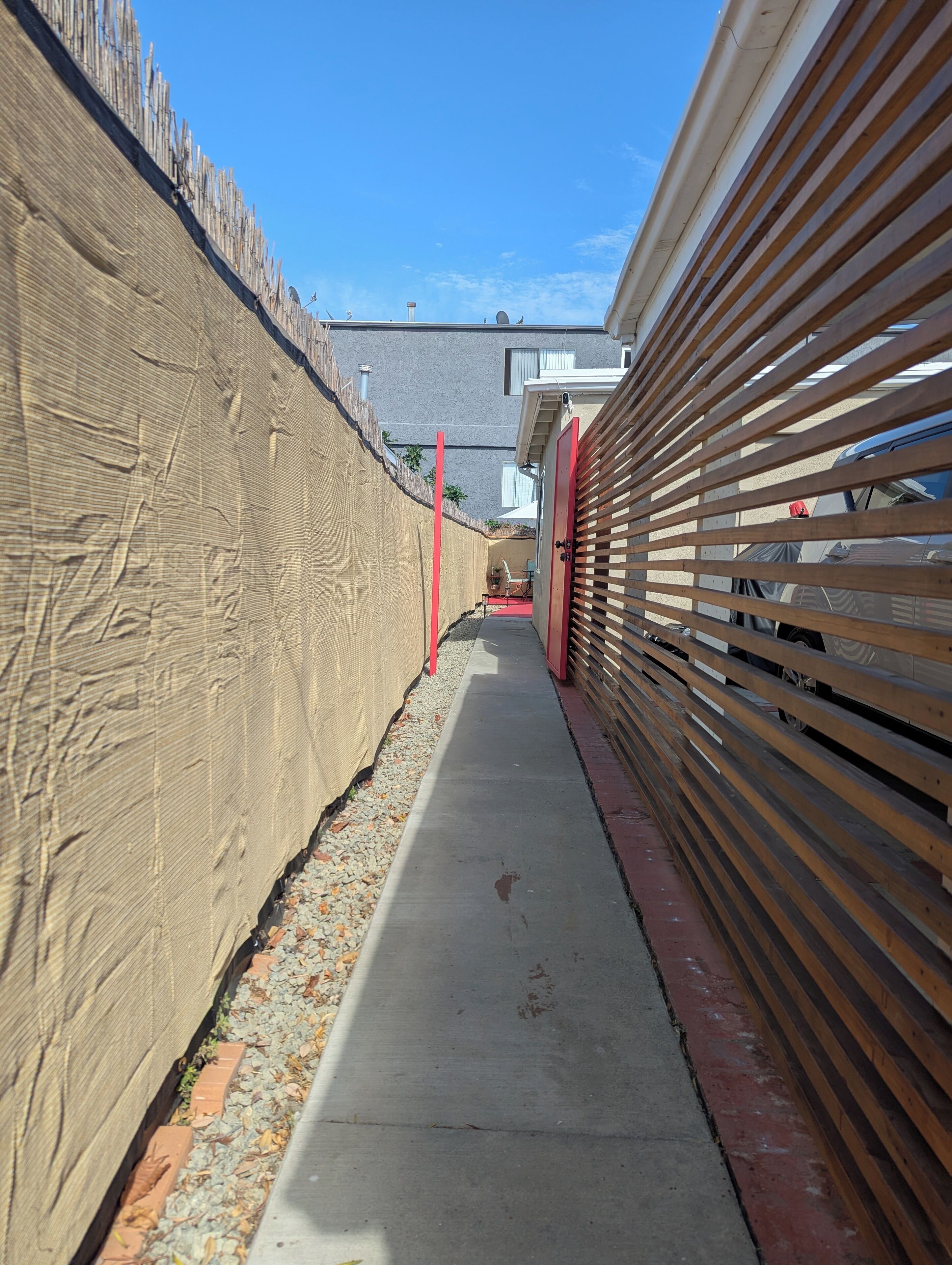 Ein schmaler Betonweg, der auf der einen Seite von einer beigen Wand und auf der anderen Seite von einem Holzzaun gesäumt wird.