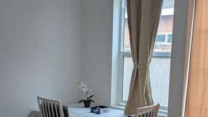 Une pièce d’angle comprenant une table à manger, deux chaises, une plante en pot et une fenêtre avec des rideaux.