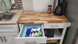 Une cuisine avec un plan de travail en bois, une machine à café, un bocal de café Nescafé et un tiroir contenant des ustensiles.