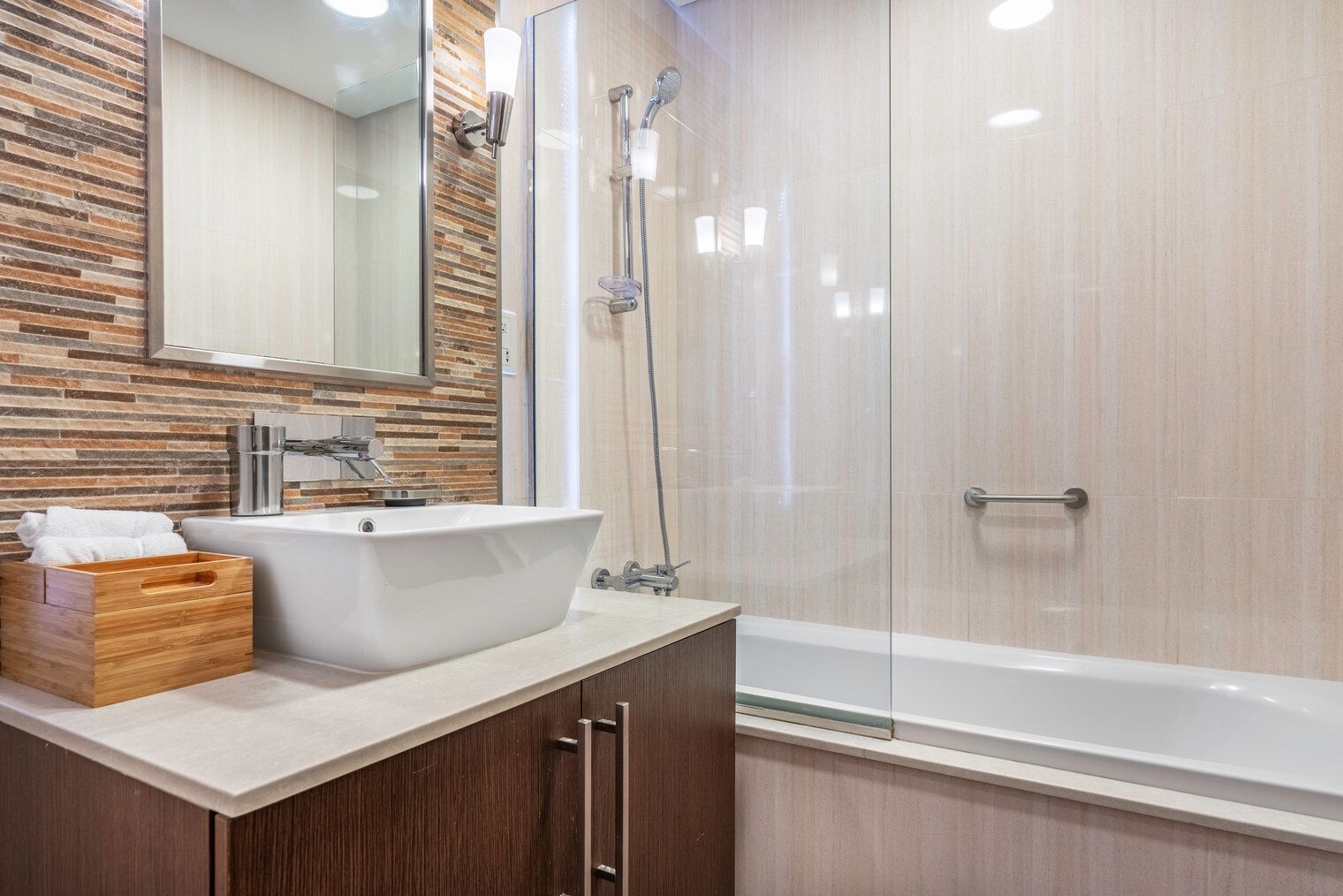 A modern bathroom with a freestanding bathtub, a glass-enclosed shower, and a wooden vanity with a sink and towel storage.
