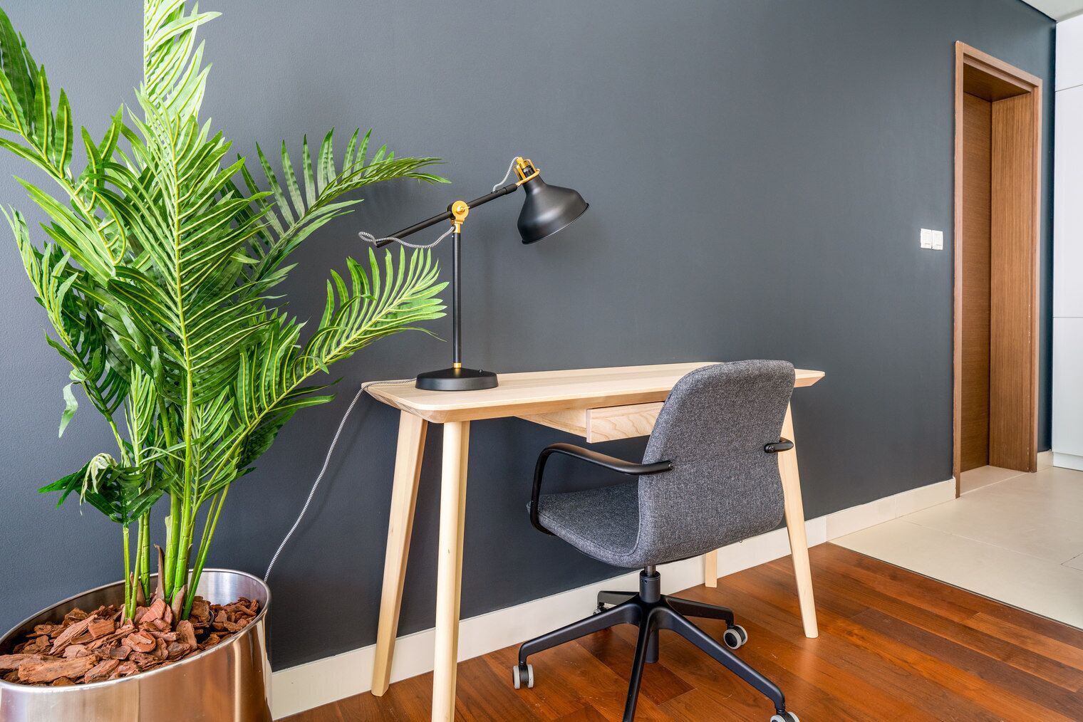 Et moderne kontor med et træskrivebord, en sort kontorstol og en potteplante.