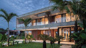 A modern two-story house with a balcony, surrounded by tropical plants and a well-maintained lawn. - Famara Villa Bali by Blacksand (Cepaka)