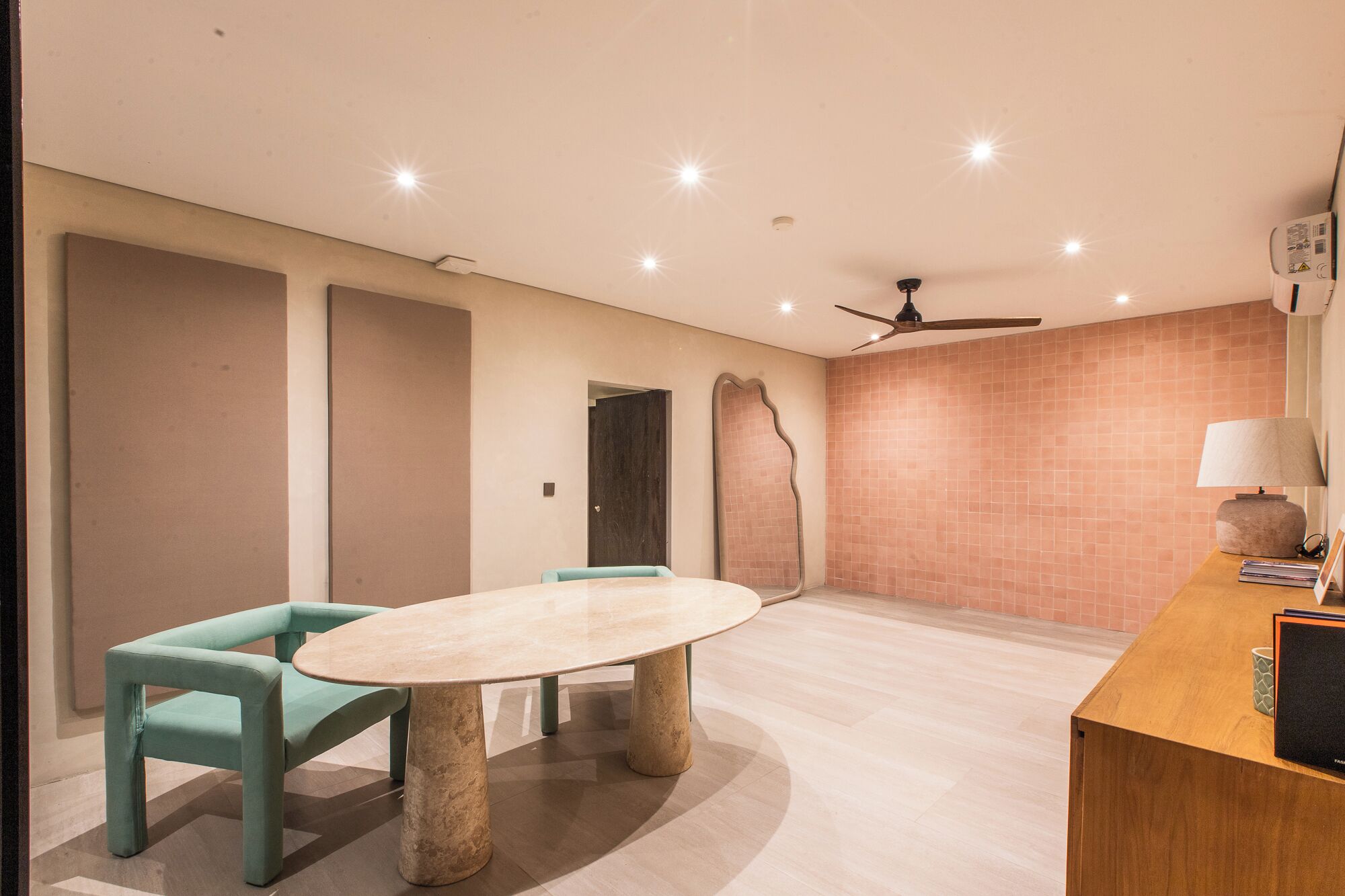 Una habitación moderna con una mesa redonda, dos sillas, un ventilador de techo y una pared con azulejos.