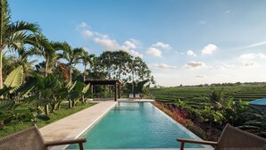 A pool with wicker chairs and a table, surrounded by lush greenery and a clear sky. - Famara Villa Bali by Blacksand (Cepaka)