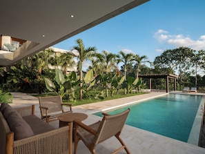 A poolside area with wicker furniture, a pergola, and lush tropical plants.