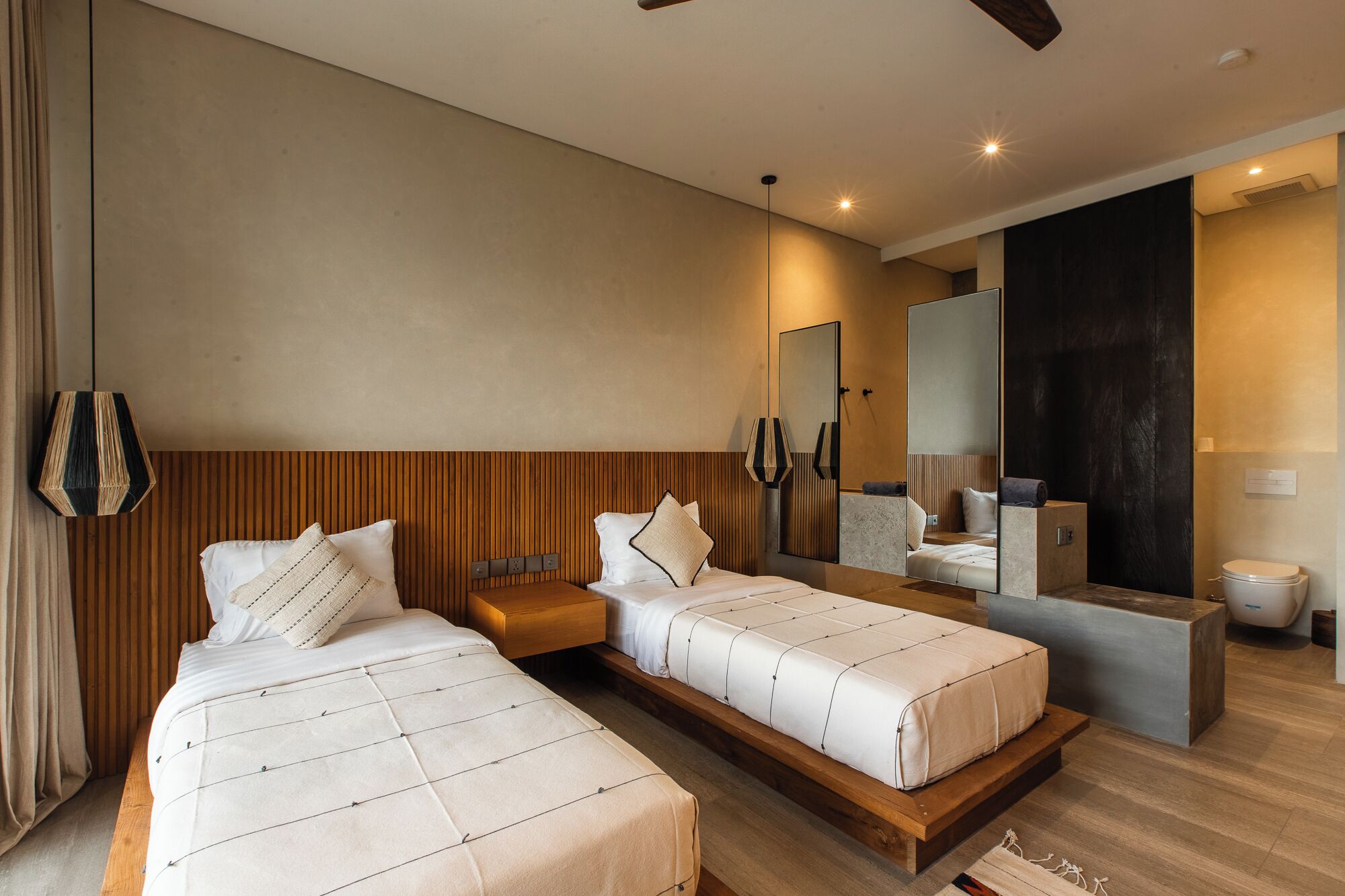 A modern hotel room with two beds, a large mirror, a vanity, and a shower area.