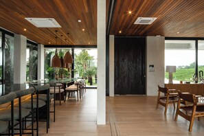 A modern interior with a wooden ceiling, large windows, and a dining area with bar stools. - Famara Villa Bali by Blacksand  (Cepaka)