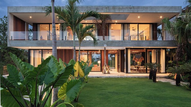 A modern two-story house with large glass windows, a flat roof, and a well-maintained garden with tropical plants. - Famara Villa Bali by Blacksand (Cepaka)