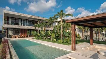 Un edificio moderno con piscina, mobiliario exterior y plantas tropicales.