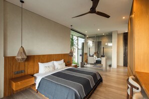 A modern bedroom with a large bed, bedside tables, a ceiling fan, and a bathroom with a mirror and sink. - Famara Villa Bali by Blacksand  (Cepaka)