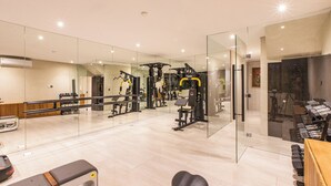 A modern gym with mirrored walls, various exercise equipment, and a bench. - Famara Villa Bali by Blacksand (Cepaka)