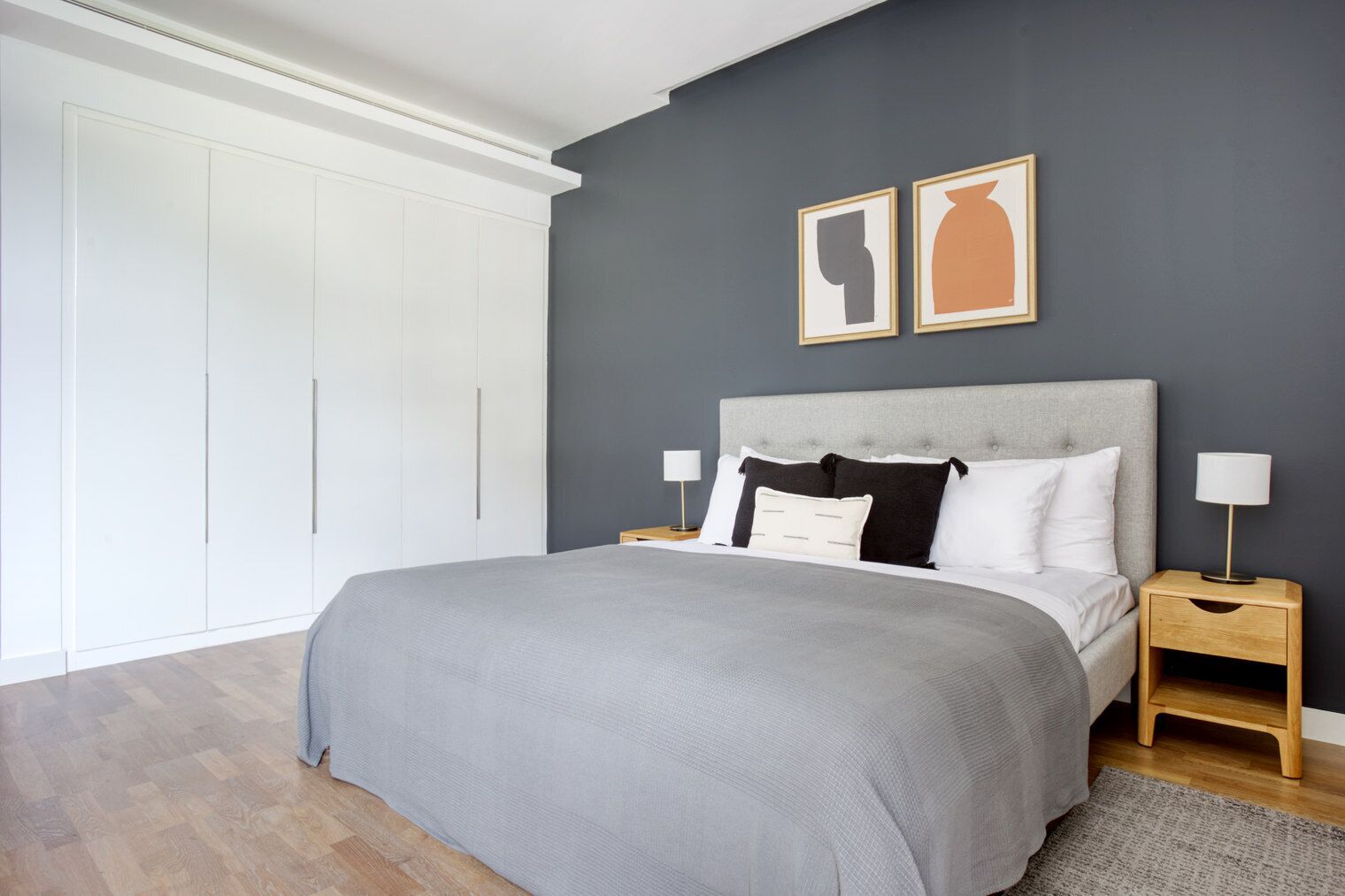 Une chambre à coucher avec un grand lit, deux tables de chevet, une armoire et deux tableaux encadrés accrochés au mur.