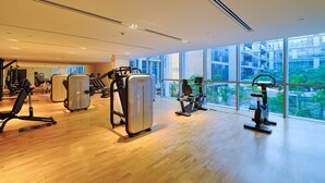 Ett modernt gym med olika typer av träningsutrustning, stora fönster och utsikt över en stadsmiljö.