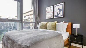 Un dormitorio moderno con una cama grande, una mesita de noche, una lámpara y dos obras de arte enmarcadas en la pared.