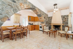 Ein Steingewölbe führt zu einer Küche mit Holzschränken, einem Essbereich mit Tisch und Stühlen sowie einem Kamin.