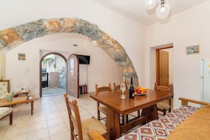 A dining area with a stone arch, wooden furniture, a television, and a fire extinguisher.