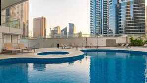Una piscina en la azotea con sillones de descanso y vistas de edificios altos aledaños.