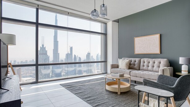 A modern living room with a large window offering a city skyline view, a grey sofa, a round coffee table, and a grey armchair.