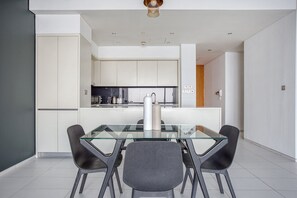 Une cuisine moderne avec des meubles blancs, une table à manger en verre et quatre chaises.