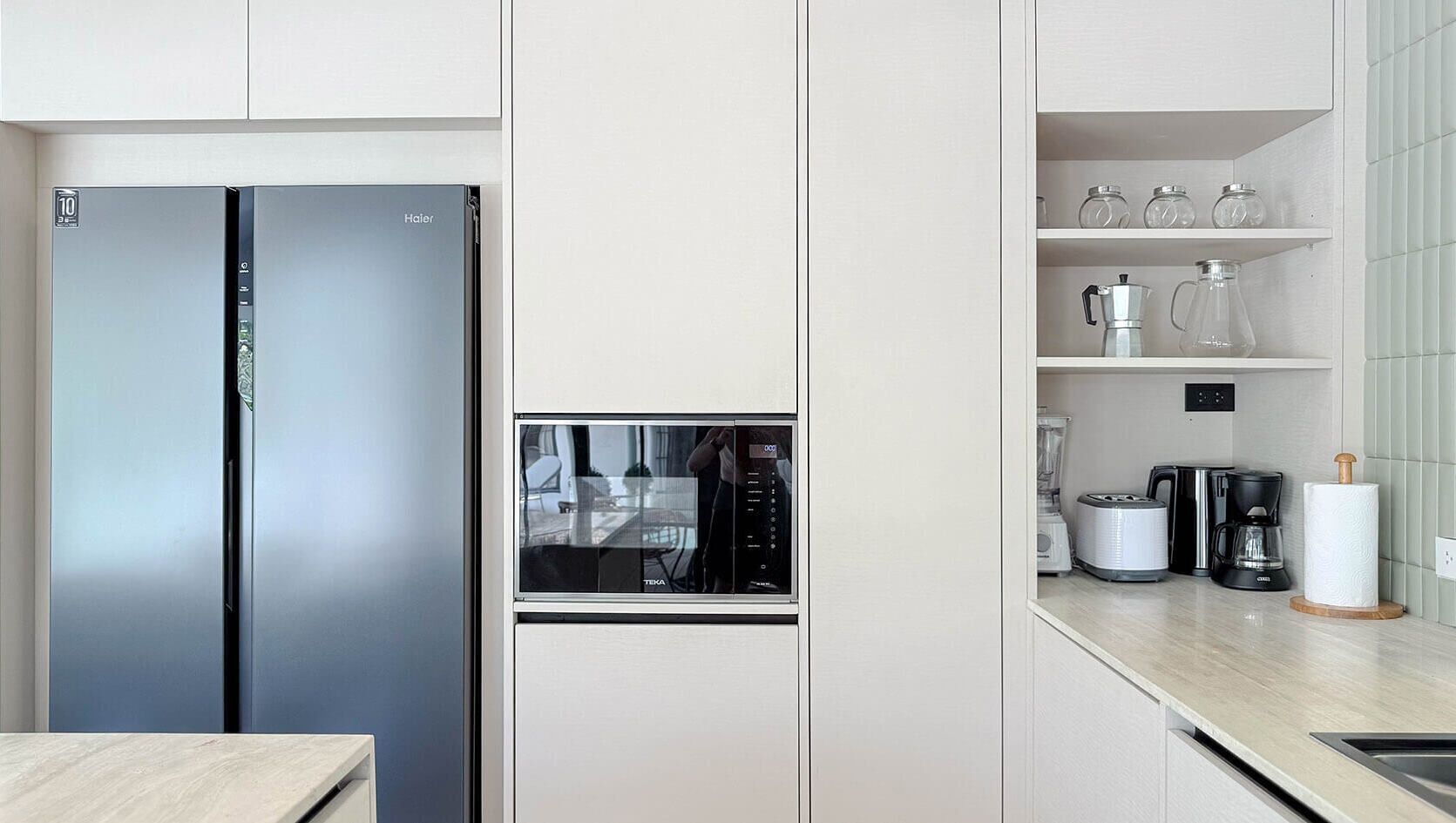 Une cuisine moderne équipée d’un réfrigérateur en acier inoxydable, d’une machine à café intégrée et d’un moulin à café posé sur le plan de travail.