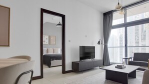 A modern living room with a sofa, coffee table, TV, and a dining area with chairs and a table. - Blueground | JLT, pool, nr Marina (Dubai)