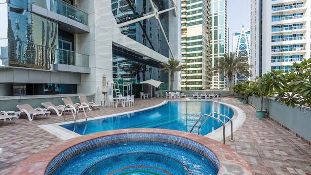 A swimming pool with lounge chairs and a hot tub, surrounded by high-rise buildings. - Blueground | JLT, pool, nr Marina (Dubai)