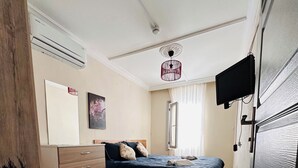 A bedroom with a bed, a dresser, a television, and an air conditioning unit. - HANCI PANSİYON (Edremit)