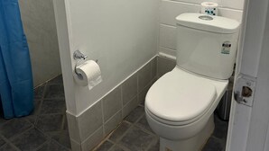 A small, white bathroom with a toilet, a roll of toilet paper, and a blue shower curtain.