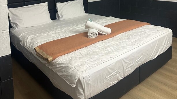 A modern hotel room with a large bed, white linens, a dark headboard, and a brown throw blanket.