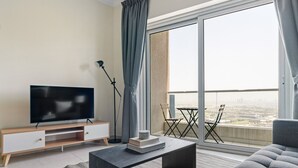 Un salon moderne avec un téléviseur à écran plat posé sur un meuble TV en bois, une table basse foncée, un canapé gris et un balcon offrant une vue sur la ville.